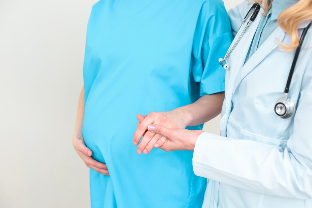 cropped shot of obstetrician gynecologist helping pregnant woman to walk and holding her hand