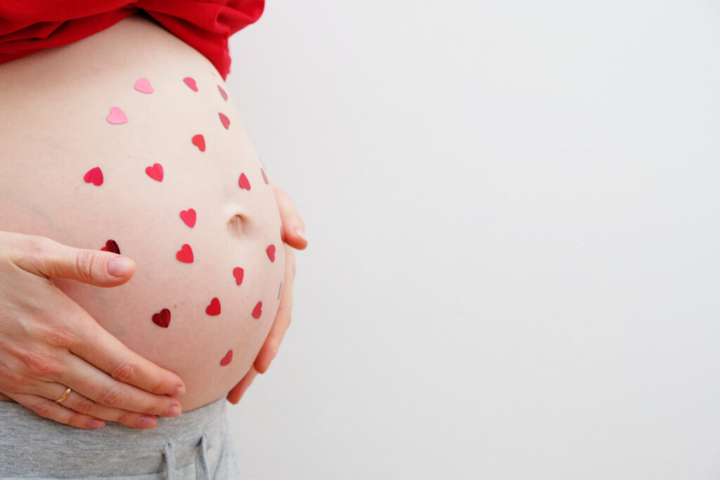 Happy Valentine's Day. A pregnant woman with heart-shaped sequins on her tummy. The concept of motherhood. Baby shower