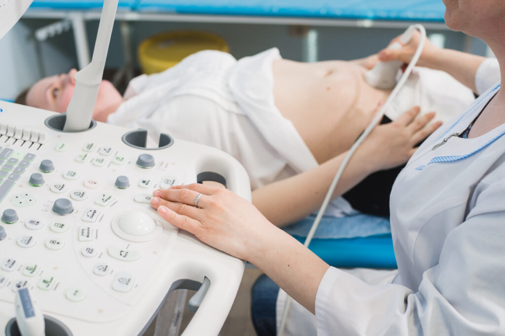 Close up of incognito doctor using ultrasound equipment for screening pregnant woman and press on buttons of special computer. Woman diagnosing in clinic.